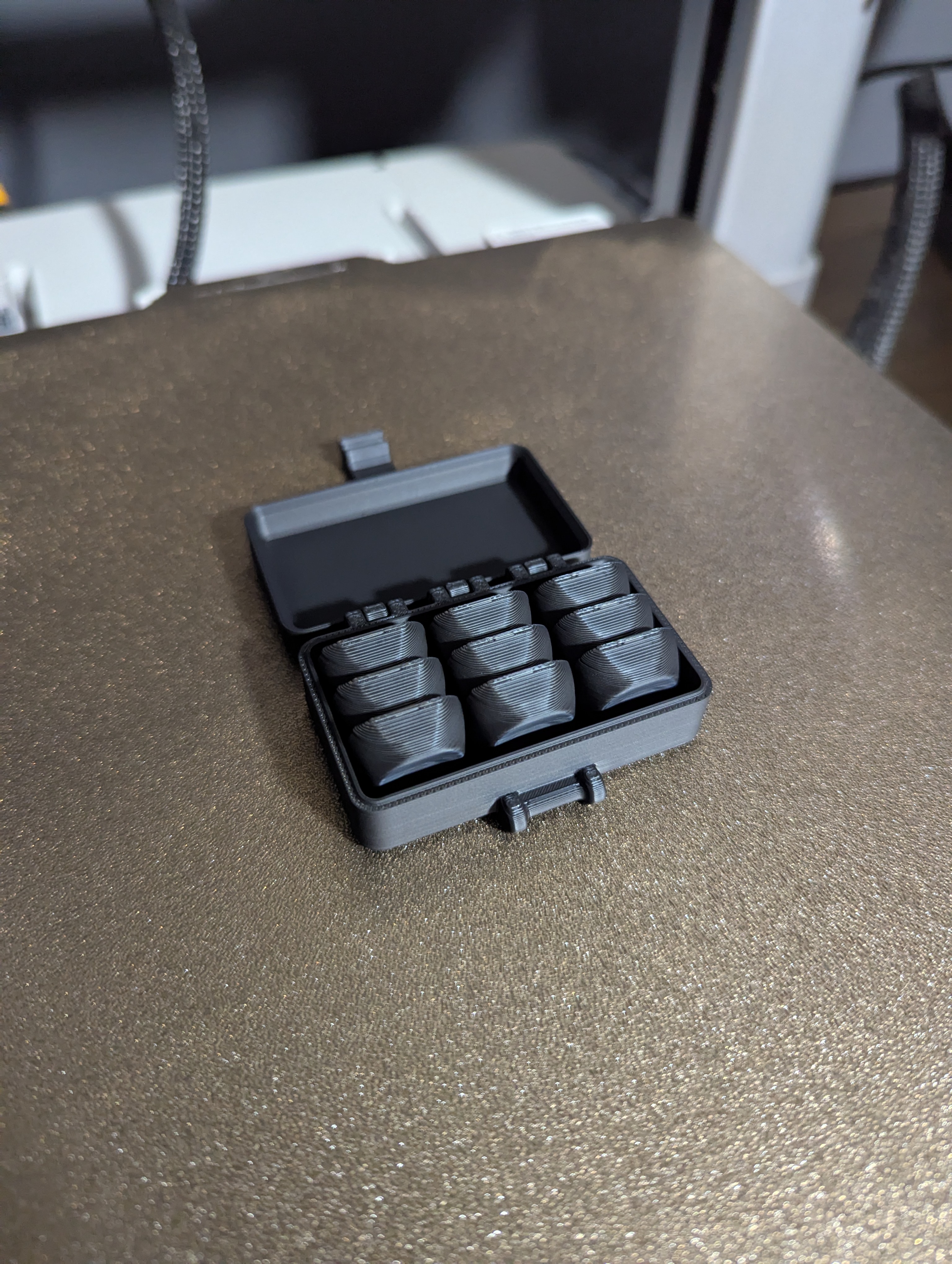 first box of caps A print in place box sitting on the printer bed used as a raft for the 9 caps perectly nestled inside in a 3 by 3 pattern.