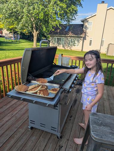 Ayla Making Pancakes on the grill in PJs Ayla wearing flowery pjs pulling pancakes off the flattop and onto a sheetpan.